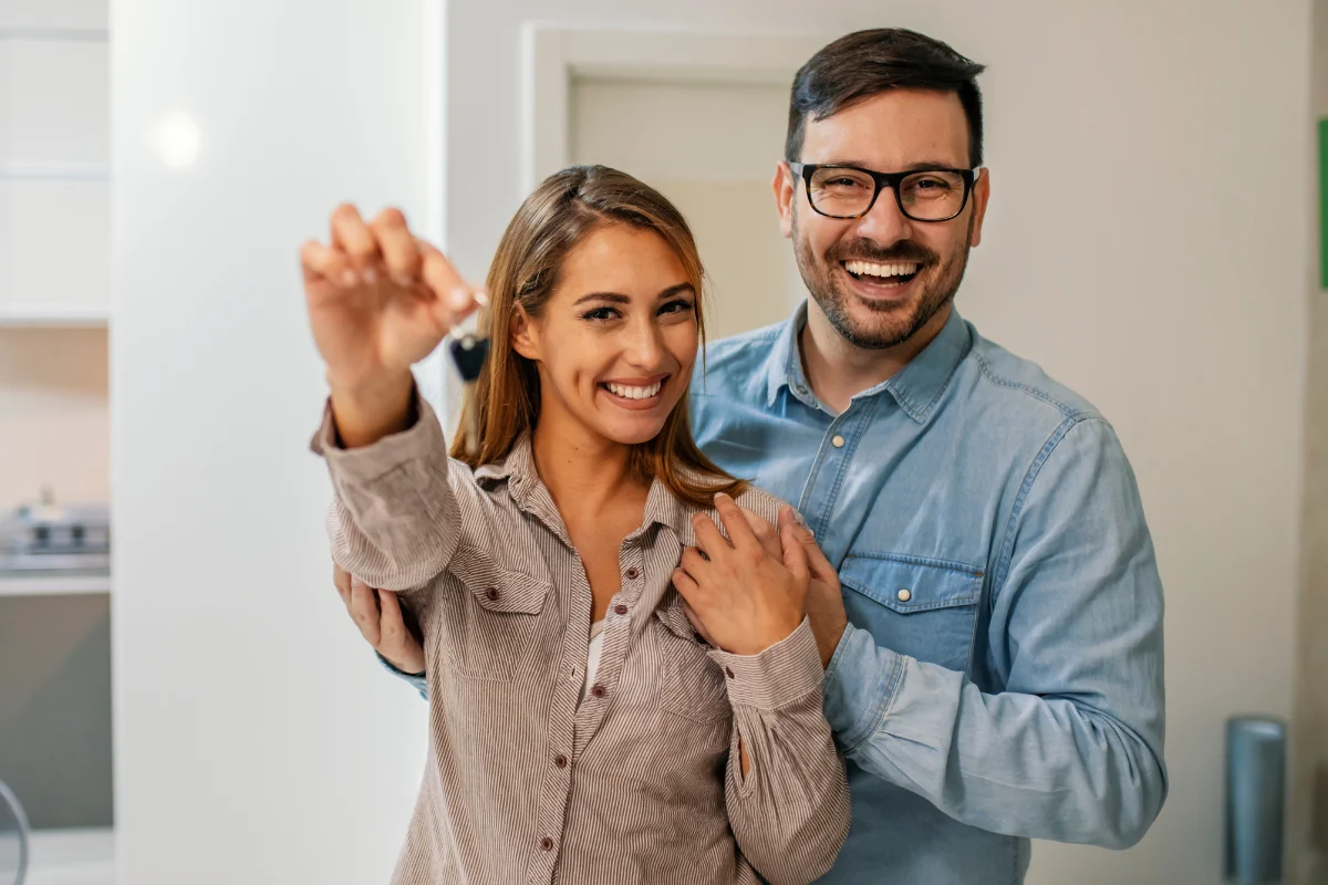 Young couple smiling in a house, with the woman holding up house keys